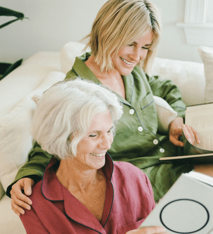Two women reading a book together on a white couch.