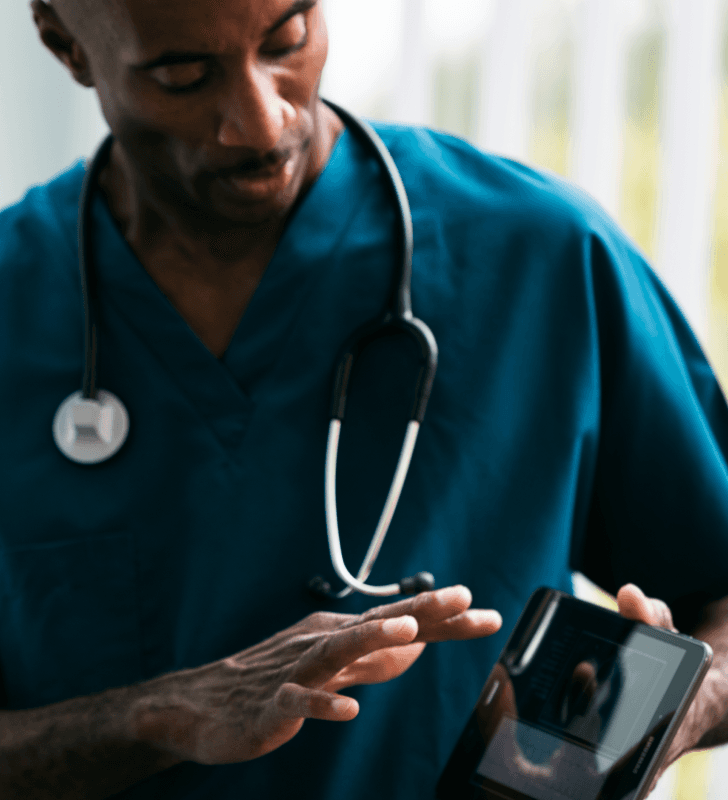Healthcare professional in scrubs with a stethoscope holding a digital tablet