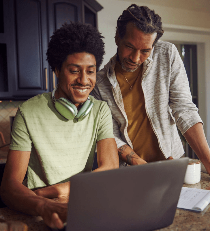 Two individuals with headphones and a laptop in a home kitchen setting.